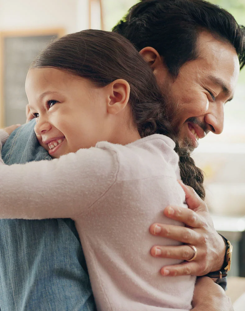 A close up shot of a man and young girl hugging each other and smiling brightly. The background is out of focus leading your eyes to the connection between the two. - Microtia Reconstruction in Seattle, WA